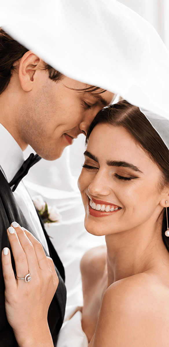 A smiling bride and groom touching foreheads beneath her veil.